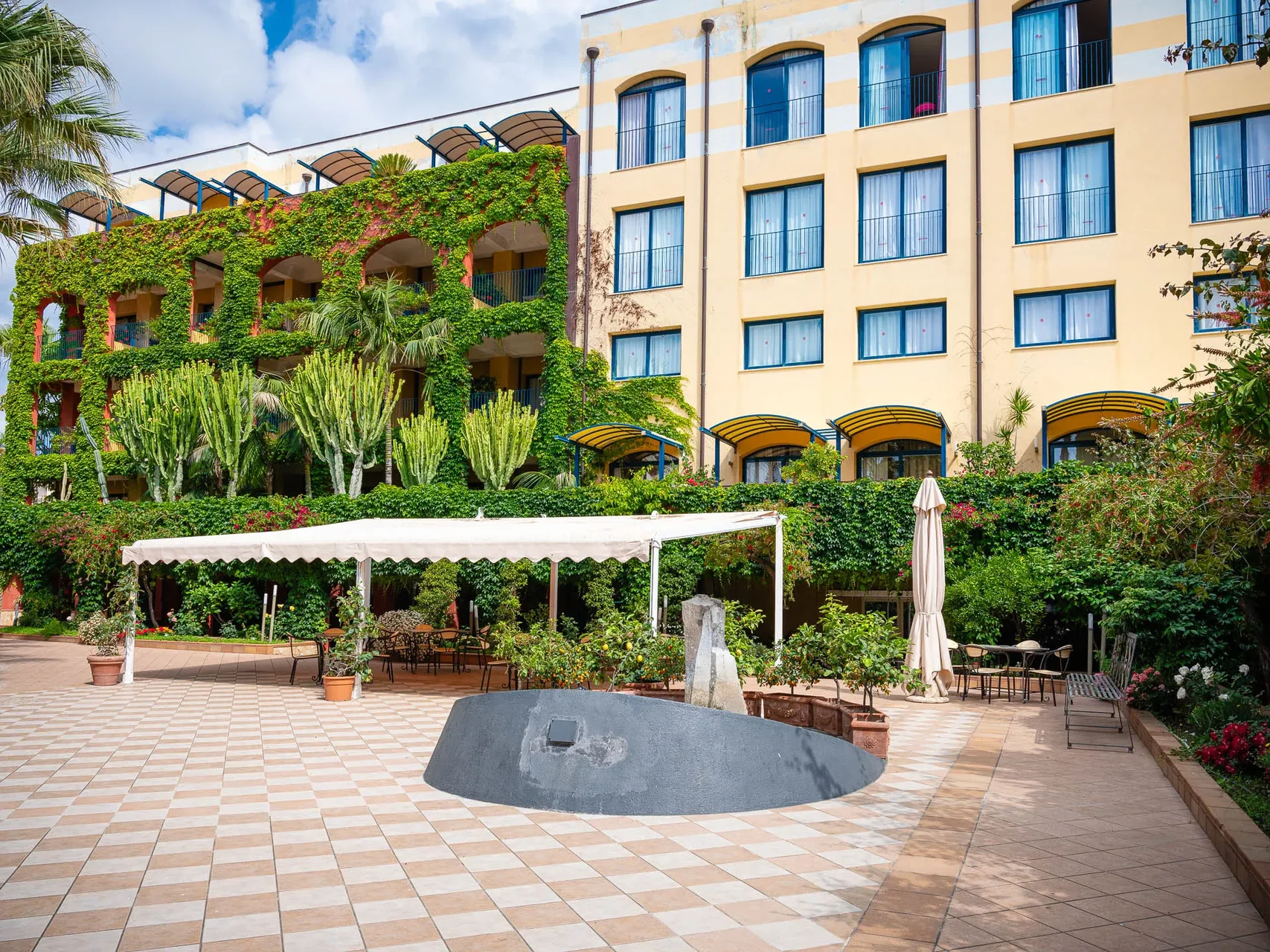 Cortile esterno dell'hotel con giardino, pergolato e facciata con edera e cactus