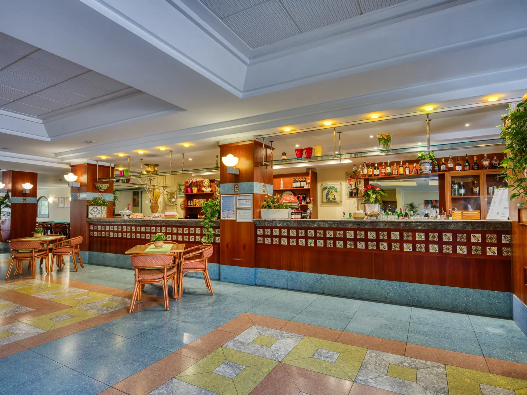 Hall dell'hotel con bancone bar in legno, piastrelle decorate e tavolini con sedie in rattan