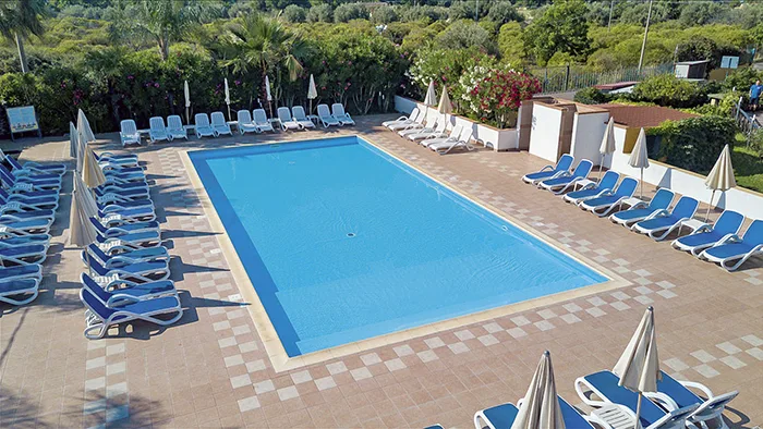 Piscina rettangolare con lettini blu circondata da vegetazione mediterranea