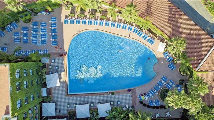 Veduta aerea della piscina a forma ovale con lettini blu e palme circostanti
