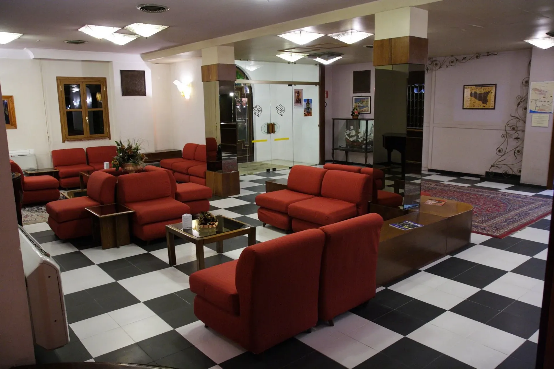 Hall con divani rossi, pavimento a scacchi bianco e nero e tappeti orientali