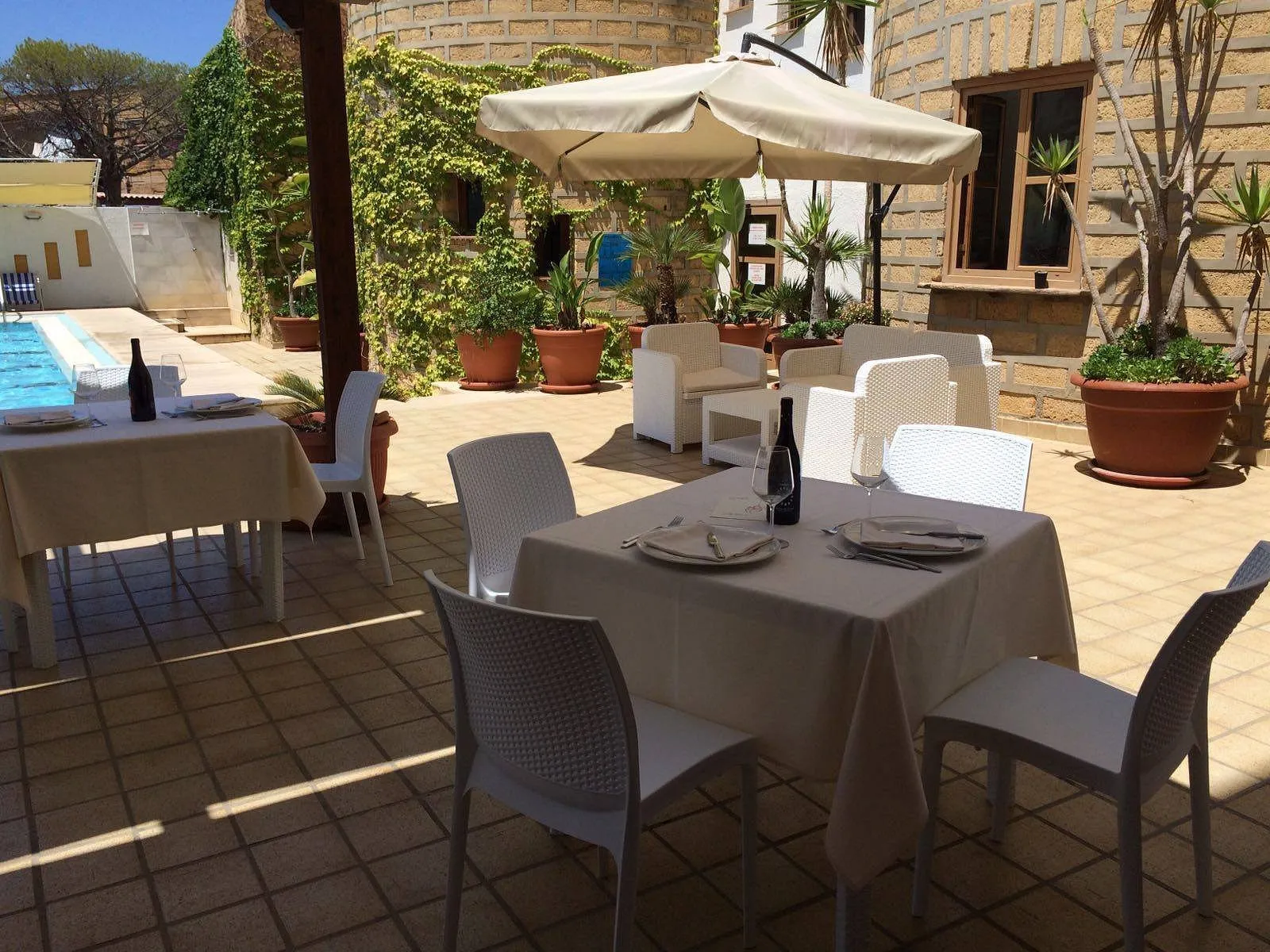 Terrazza esterna con tavoli apparecchiati sotto ombrellone accanto alla piscina
