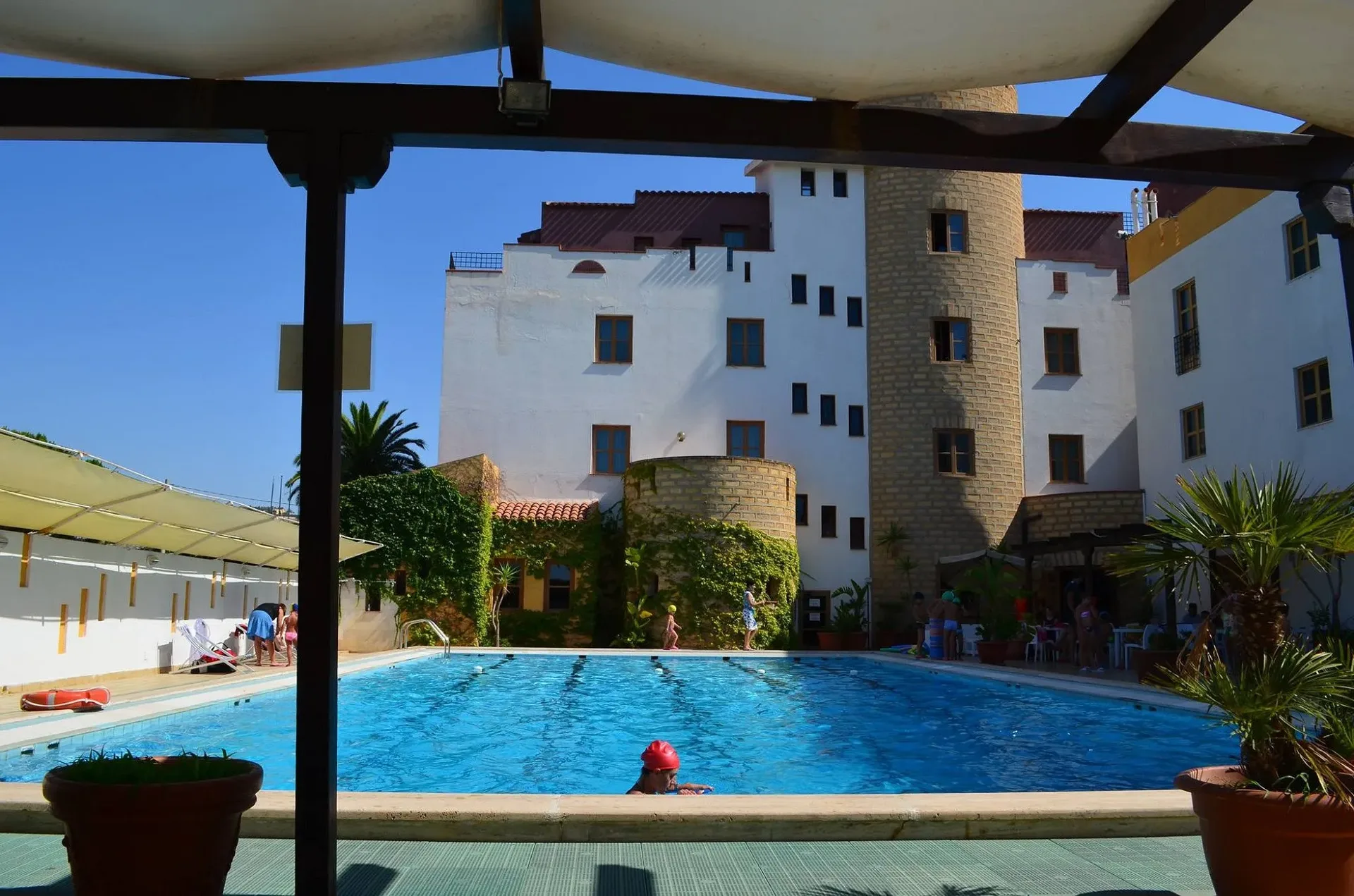 Piscina esterna con ospiti in acqua e vista sulla torre in pietra dell'hotel