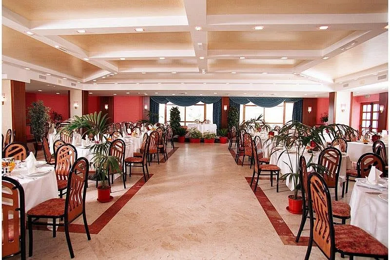 Ampia sala ristorante con tavoli apparecchiati in bianco e piante decorative