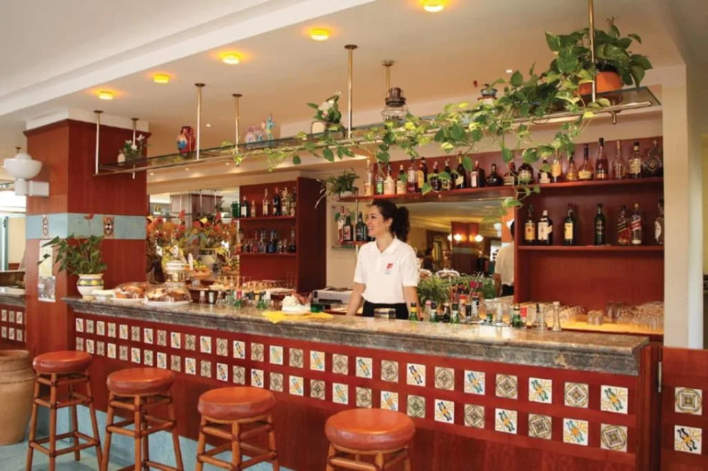 Bancone del bar in legno con piastrelle decorate, barista e ampia selezione di bottiglie sullo sfondo