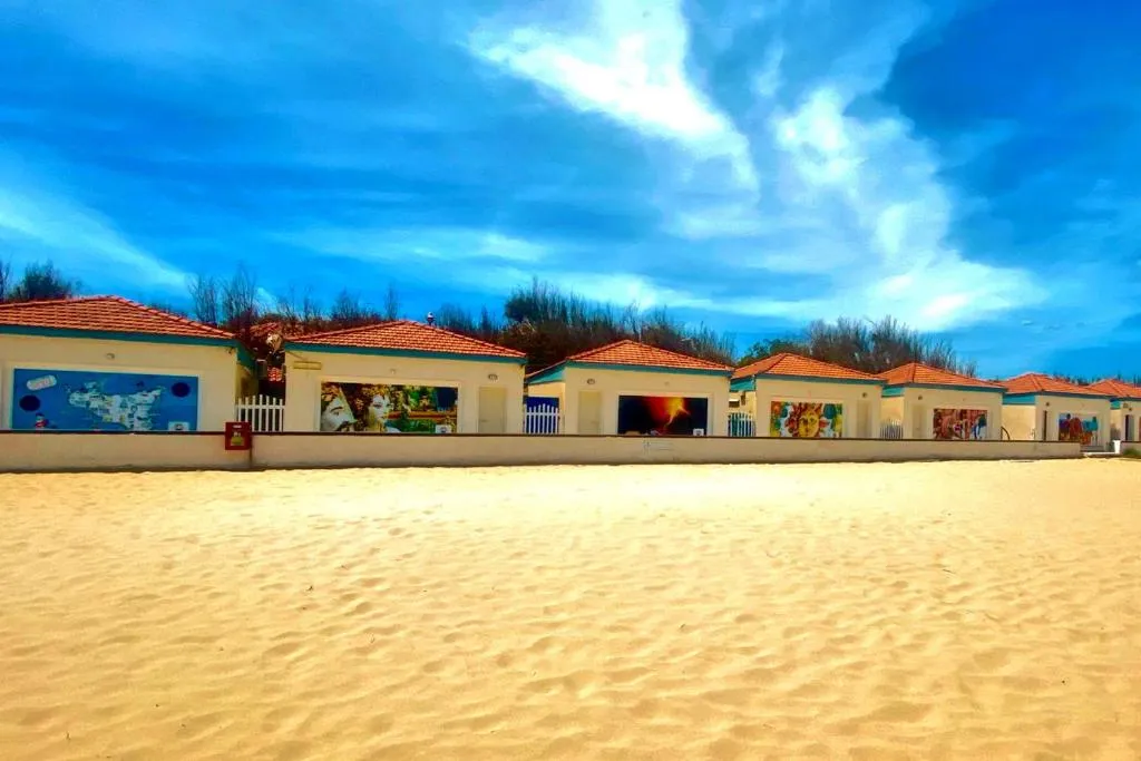 Fila di cabine bianche con murales artistici sulla spiaggia sotto cielo nuvoloso