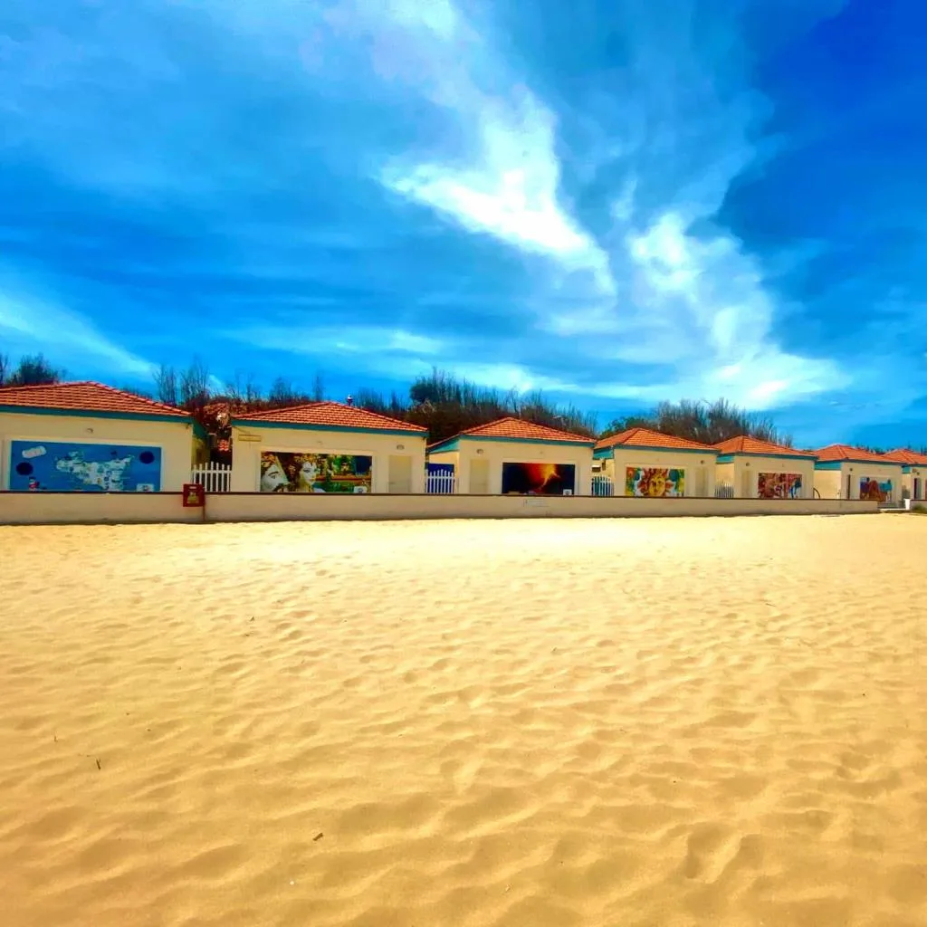 Fila di cabine sulla spiaggia con murales colorati sotto cielo azzurro