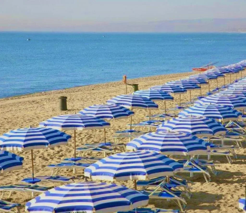 File di ombrelloni a righe blu e bianche con lettini sulla spiaggia vista mare