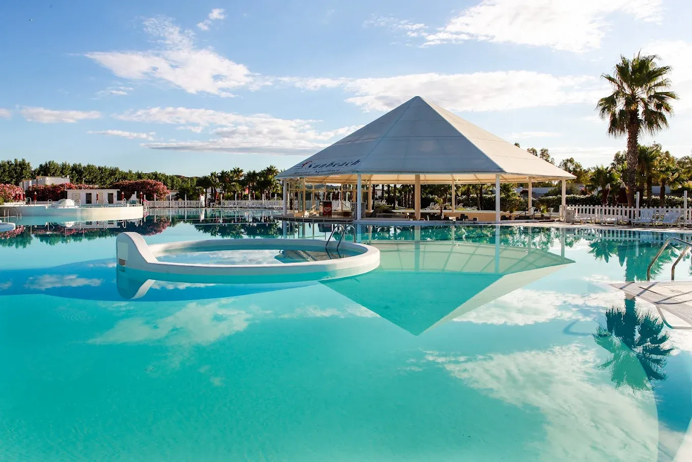 Ampia piscina con gazebo bianco a piramide riflesso nell'acqua e palme