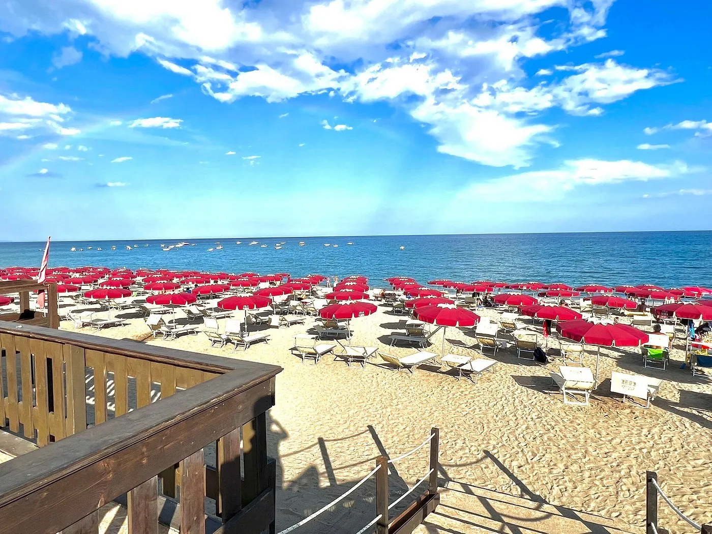 Spiaggia con file di ombrelloni rossi e lettini affacciata sul mare azzurro