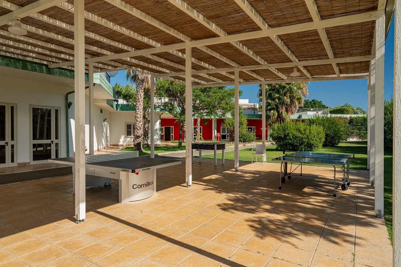 Area giochi coperta con tavoli da ping pong e calcio balilla tra le palme