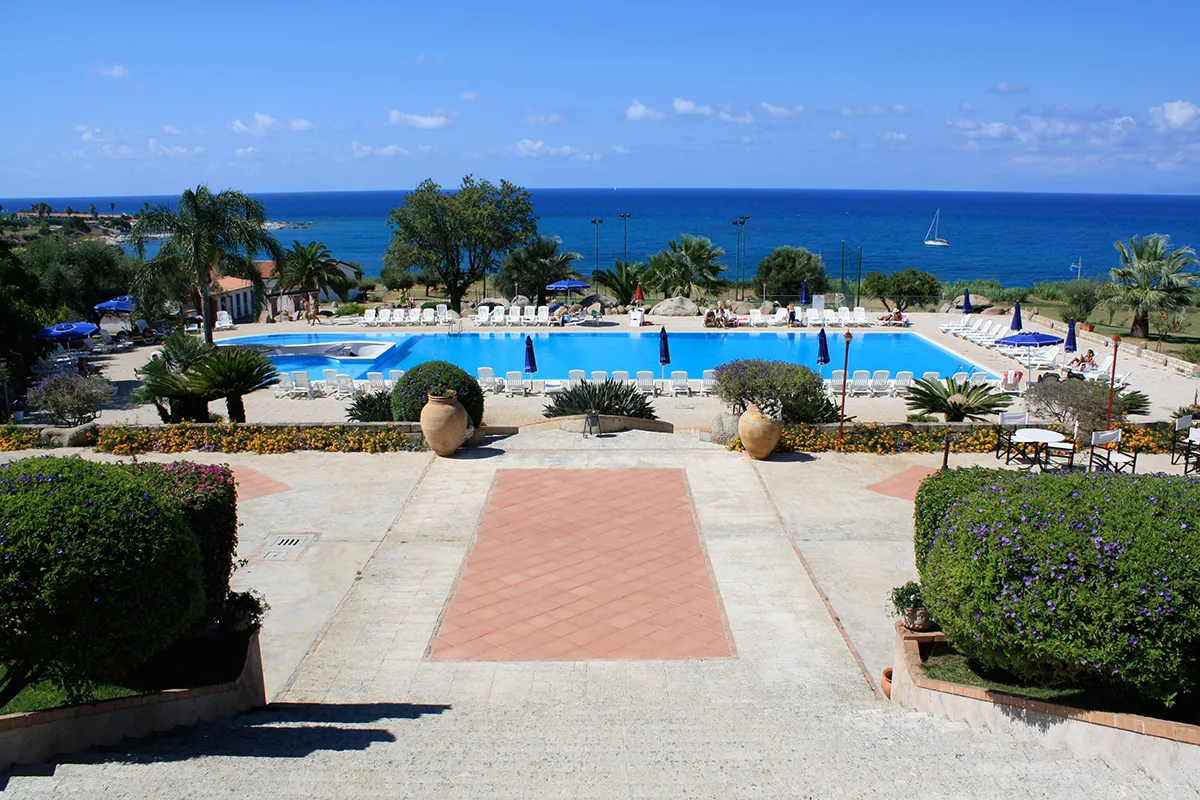 Piscina rettangolare con lettini bianchi e vista sul mare e barca a vela