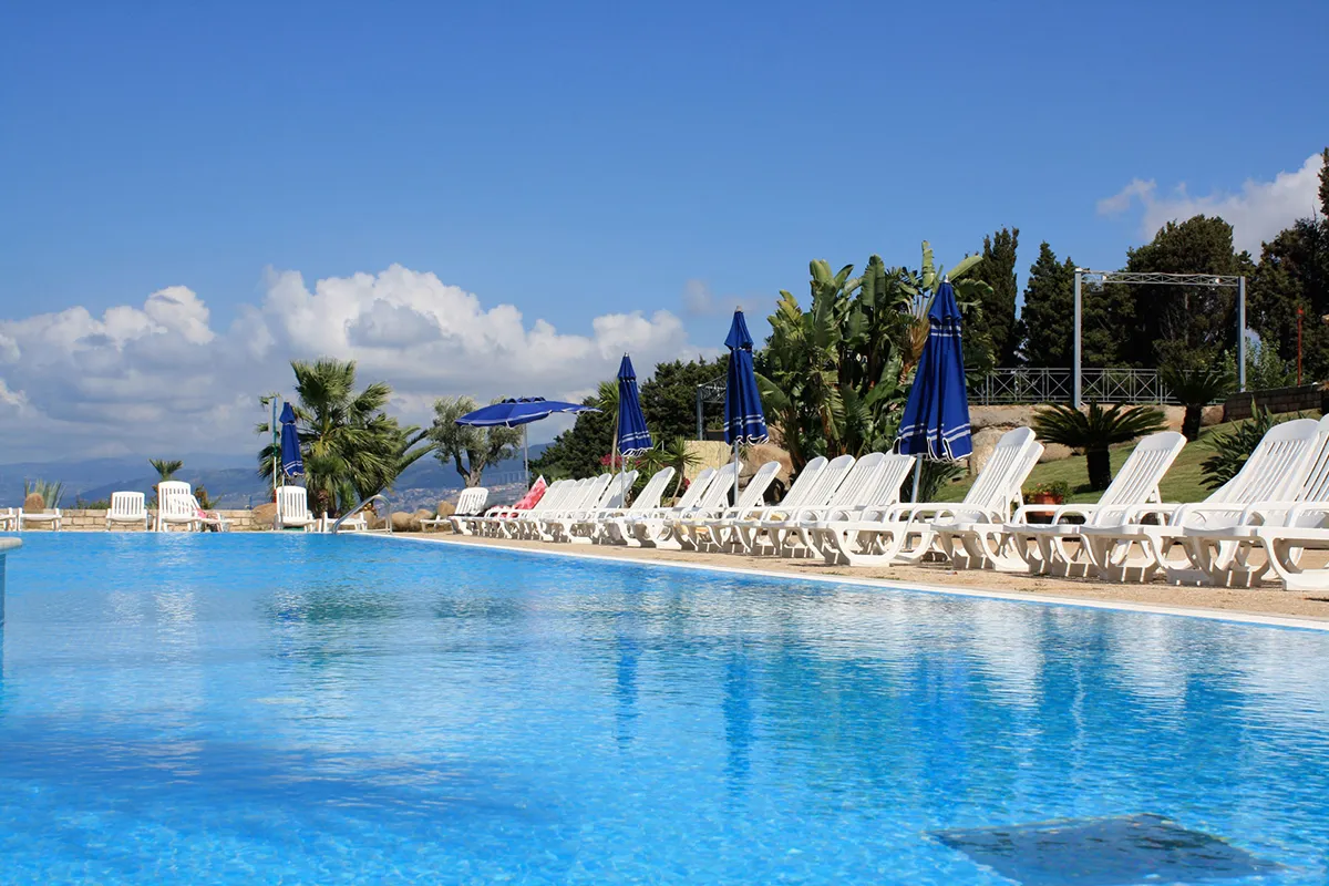 Bordo piscina con lettini bianchi e ombrelloni blu chiusi