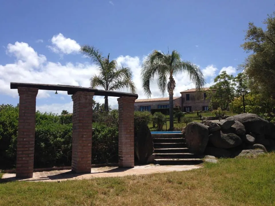 Giardino con pergolato in mattoni, palme e casale sullo sfondo