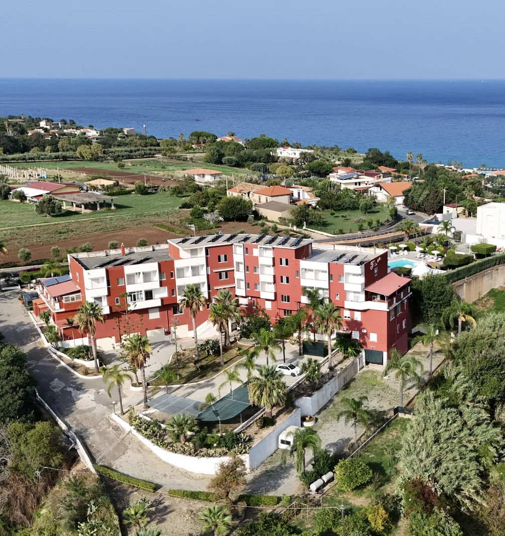 Vista aerea dell'hotel rosso e bianco circondato da palme con il mare e la campagna sullo sfondo