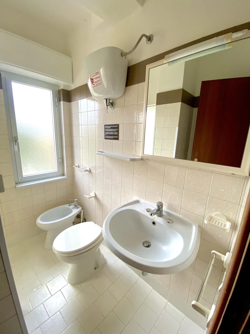 Bagno piastrellato con lavabo, WC, bidet, specchio e finestra