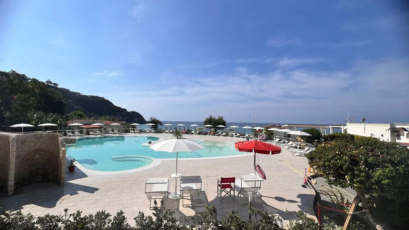 Ampia piscina con ombrelloni e lettini affacciata sul mare