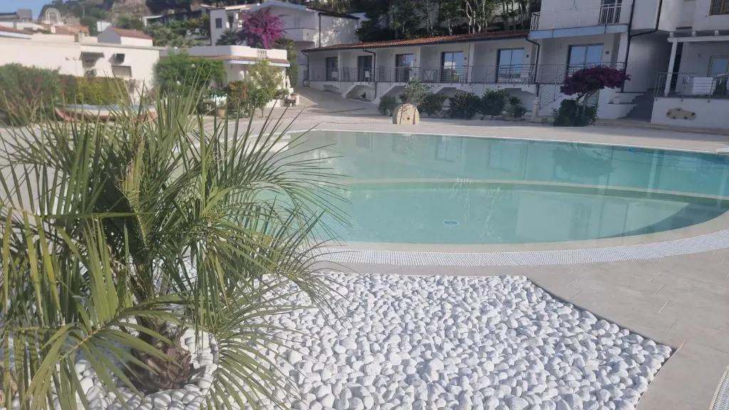 Piscina con bordo in ciottoli bianchi e palma, circondata da edifici residenziali