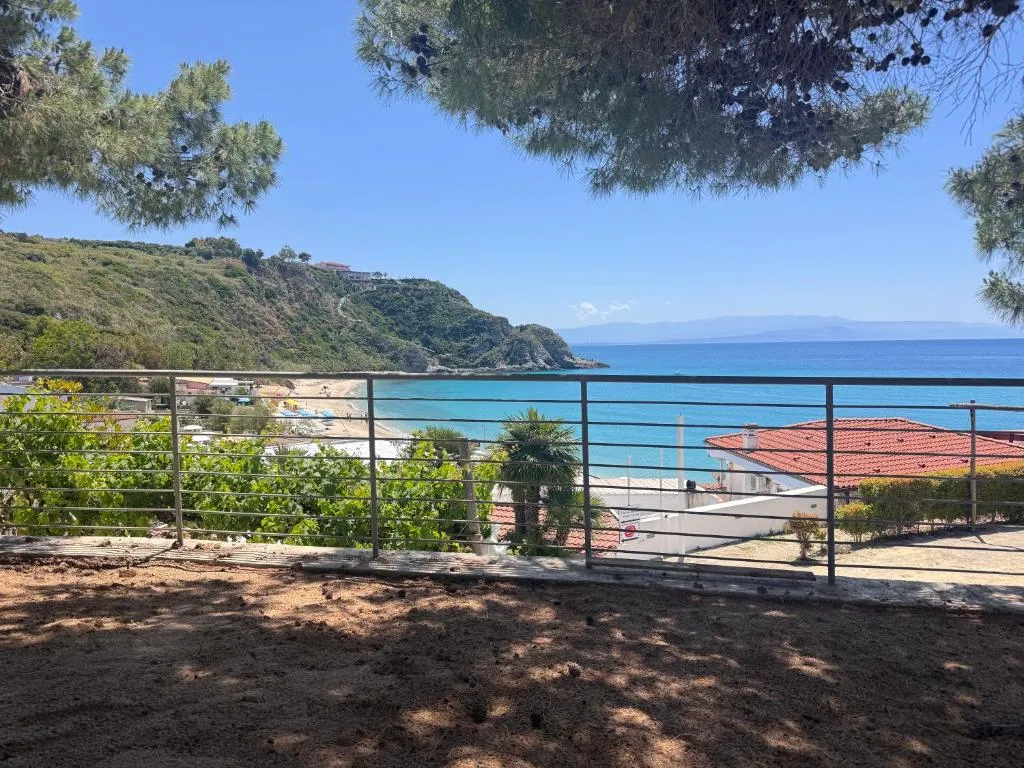 Vista sul mare e sulla spiaggia da una terrazza con ringhiera tra alberi di pino
