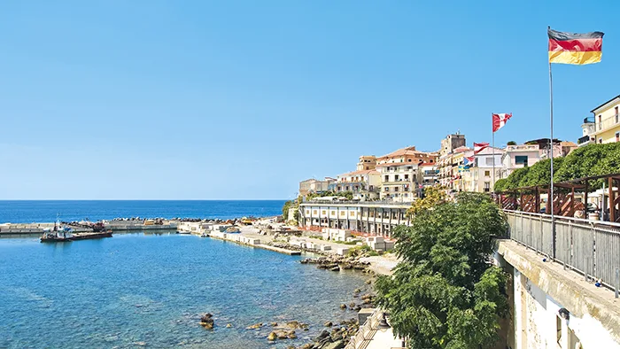 Vista del borgo costiero con porticciolo, edifici storici e bandiere sul lungomare