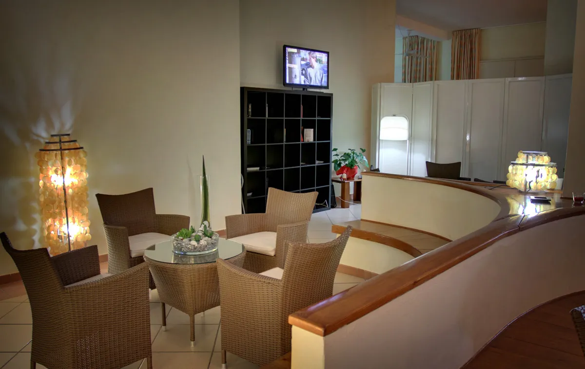Hall dell'hotel con poltrone in vimini, reception e televisore