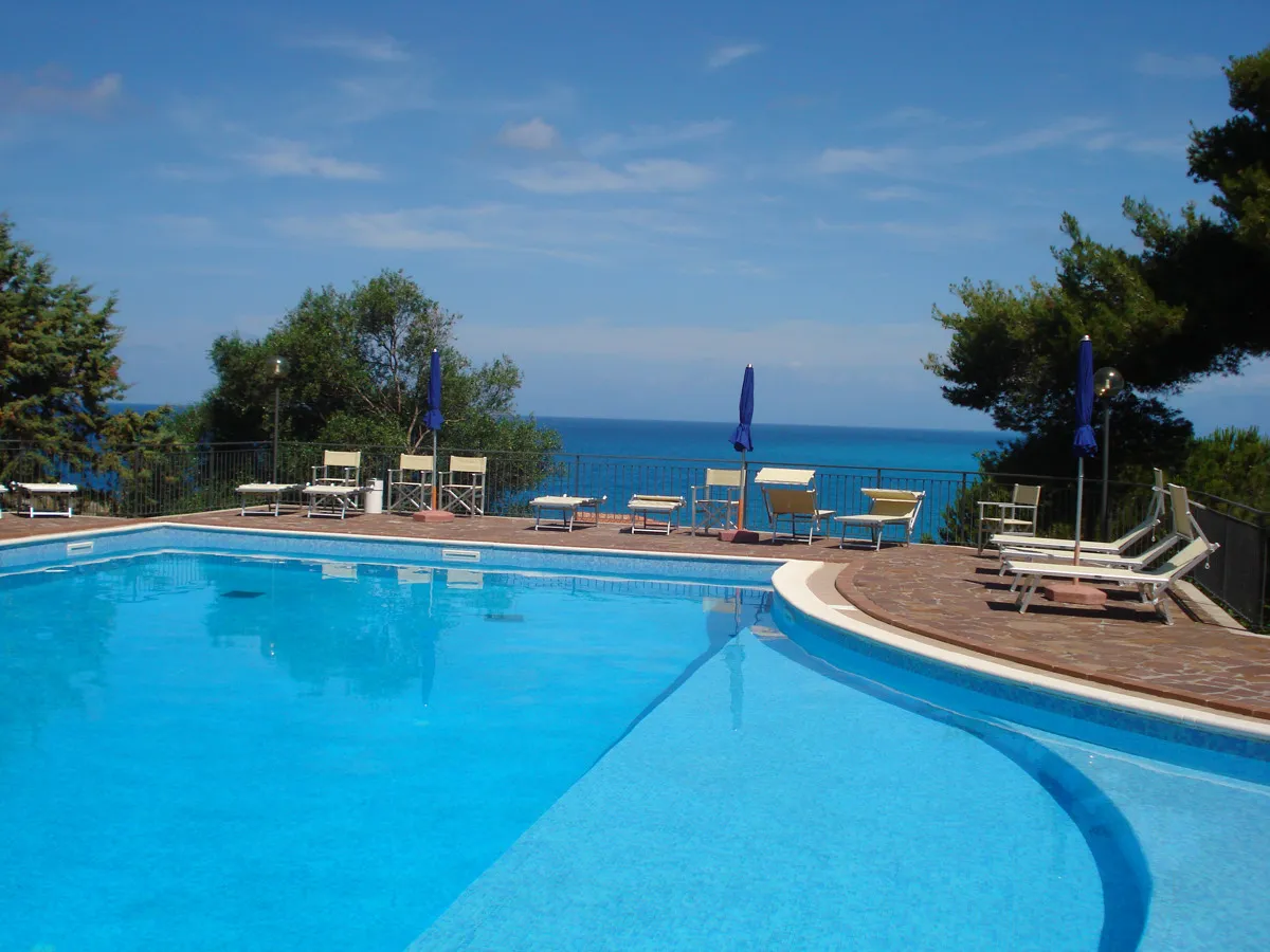 Piscina all'aperto con lettini, ombrelloni blu e vista panoramica sul mare