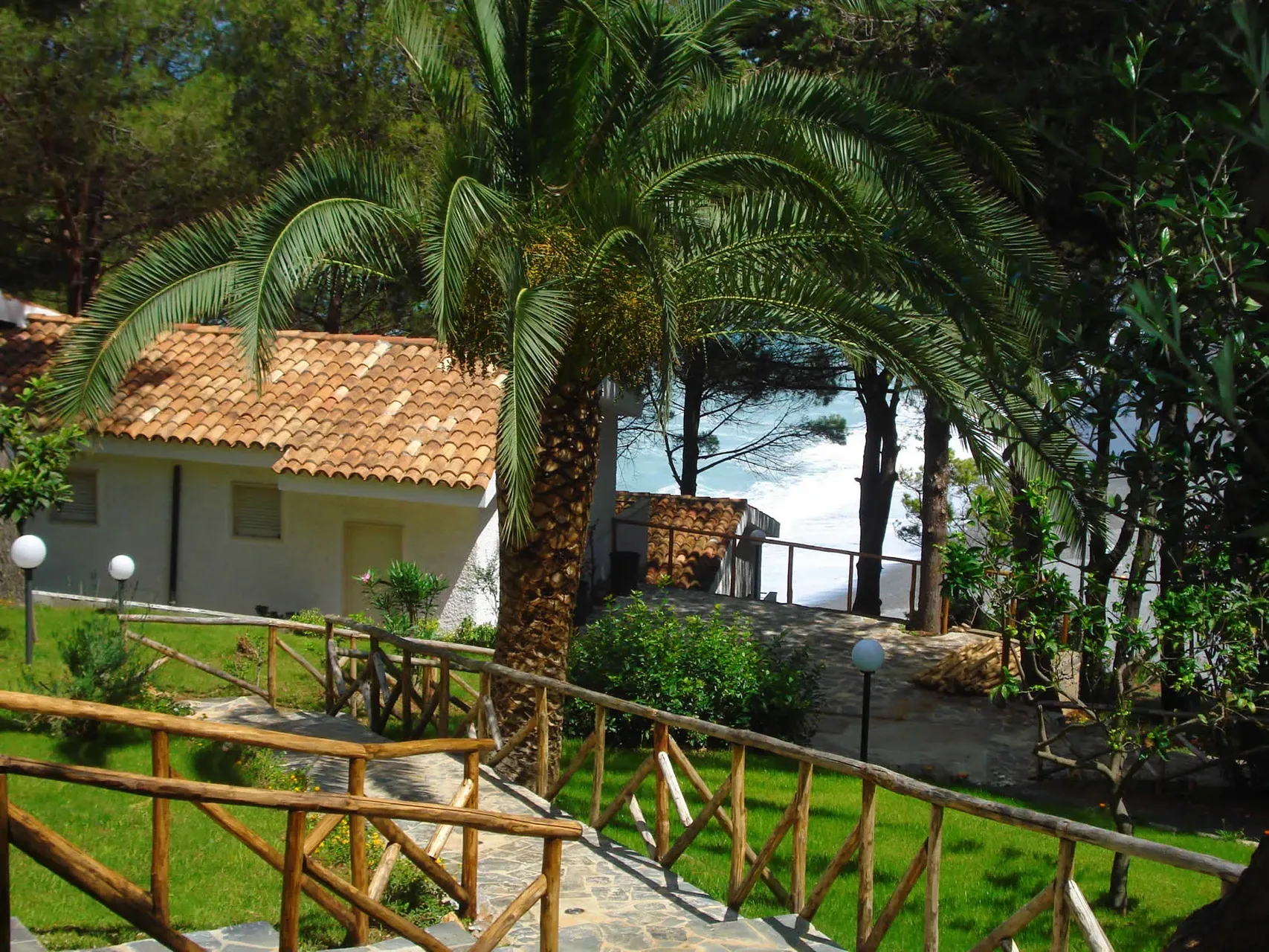 Vialetto in pietra tra palme e giardino con vista sul mare e cottage