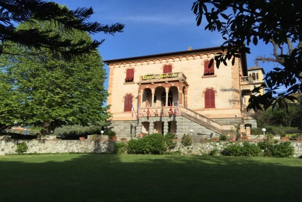 Vista della villa storica con giardino verde alberato e cielo azzurro