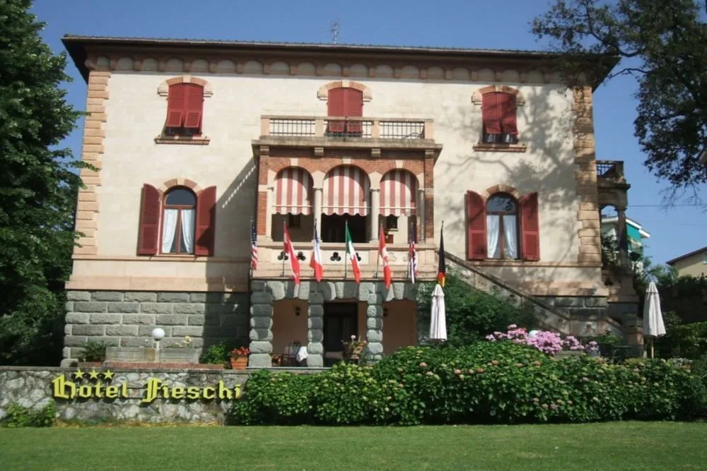 Facciata dell'Hotel Fieschi con bandiere, portico ad archi e giardino fiorito