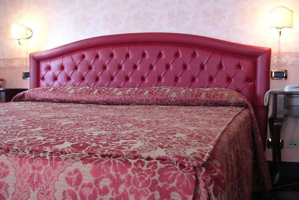 Dettaglio letto matrimoniale con testiera capitonné rossa e copriletto damascato