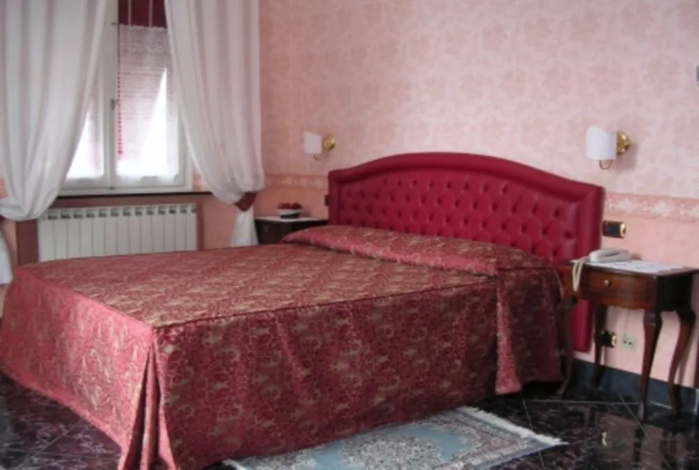 Camera matrimoniale con testiera imbottita rossa, tende bianche e comodino in legno