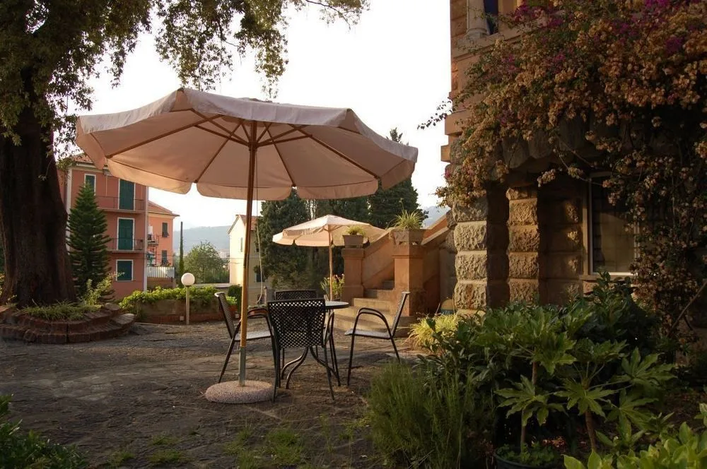 Terrazza esterna con tavolo, sedie e ombrellone tra piante fiorite al tramonto
