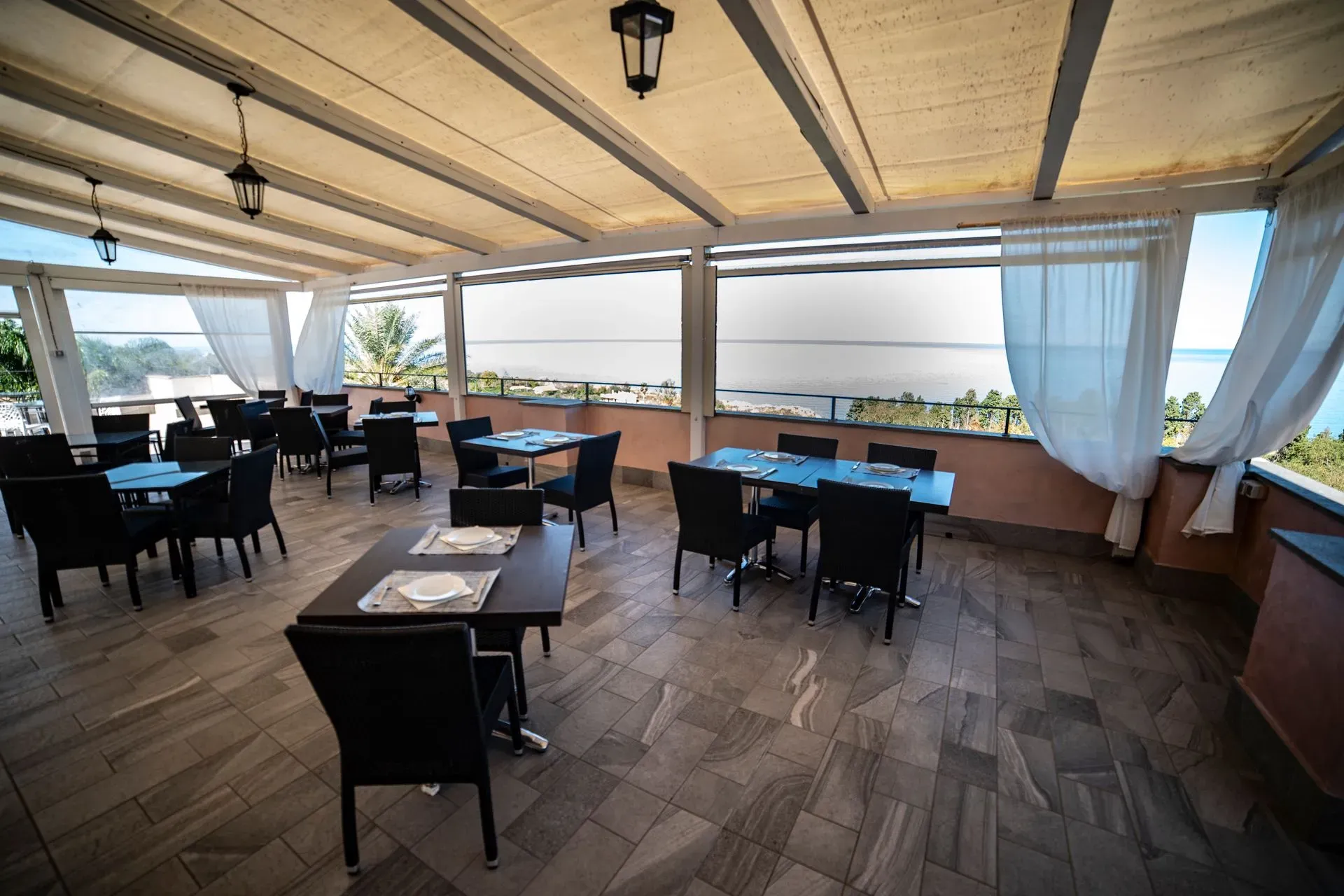 Sala ristorante coperta con tende bianche e vista panoramica sul mare