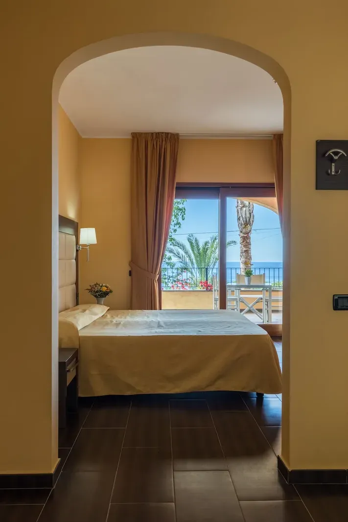 Camera matrimoniale con arco, porta finestra e vista mare con palma