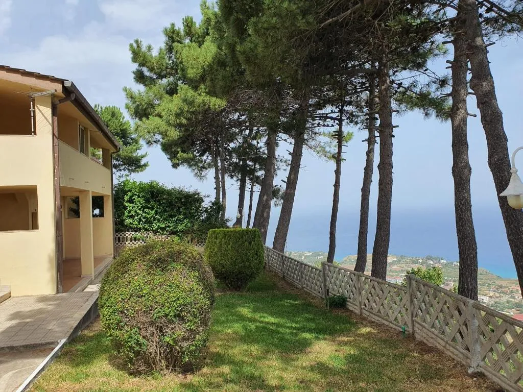 Giardino con pini, siepi e vista sul mare accanto a un edificio del resort