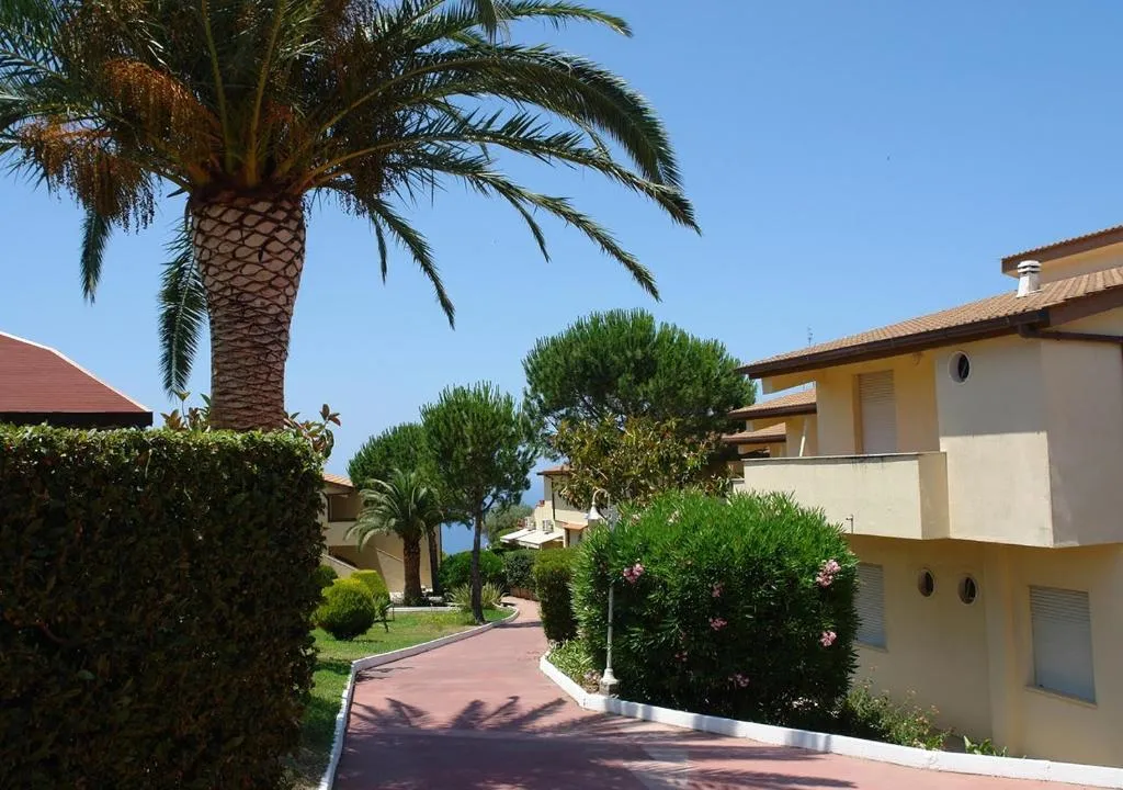 Viale pedonale del resort con palme, siepi fiorite ed edifici color giallo
