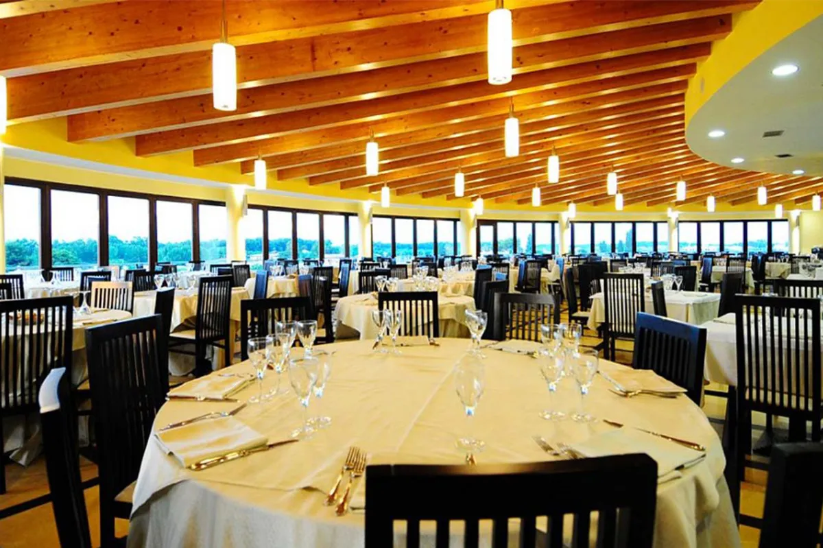 Ristorante interno con tavoli rotondi apparecchiati e soffitto a travi in legno