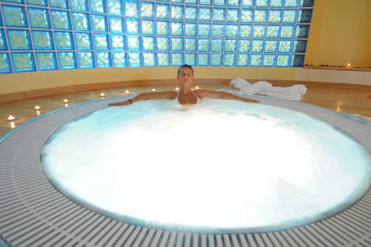 Vasca idromassaggio rotonda della spa con persona in relax e pareti in vetrocemento