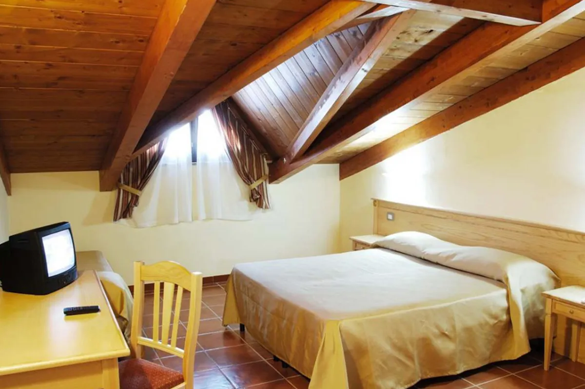 Camera mansardata con soffitto in legno a travi, letto matrimoniale e scrivania