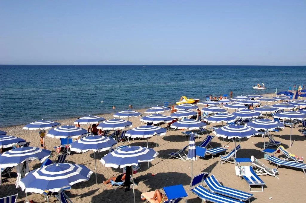 Spiaggia attrezzata con ombrelloni e lettini bianchi e blu davanti al mare