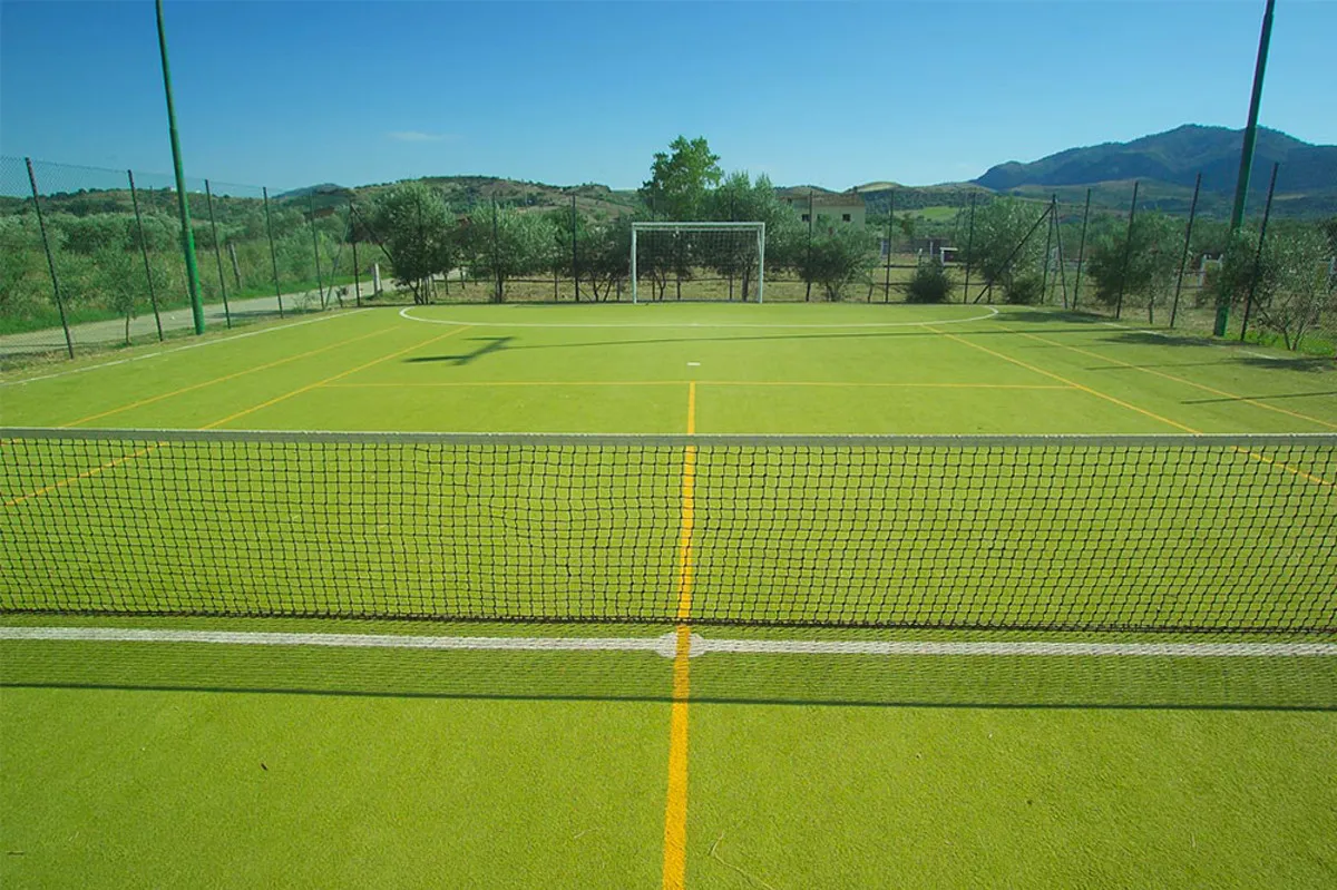 Campo sportivo in erba sintetica con rete e porta da calcio tra le colline