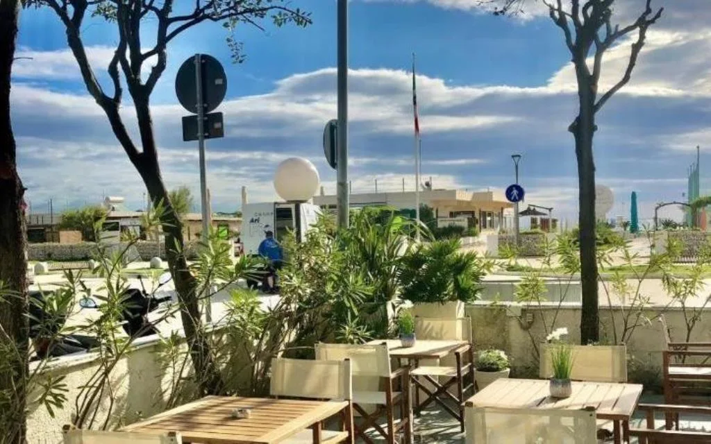 Terrazza esterna con tavolini in legno e vista sul lungomare al tramonto
