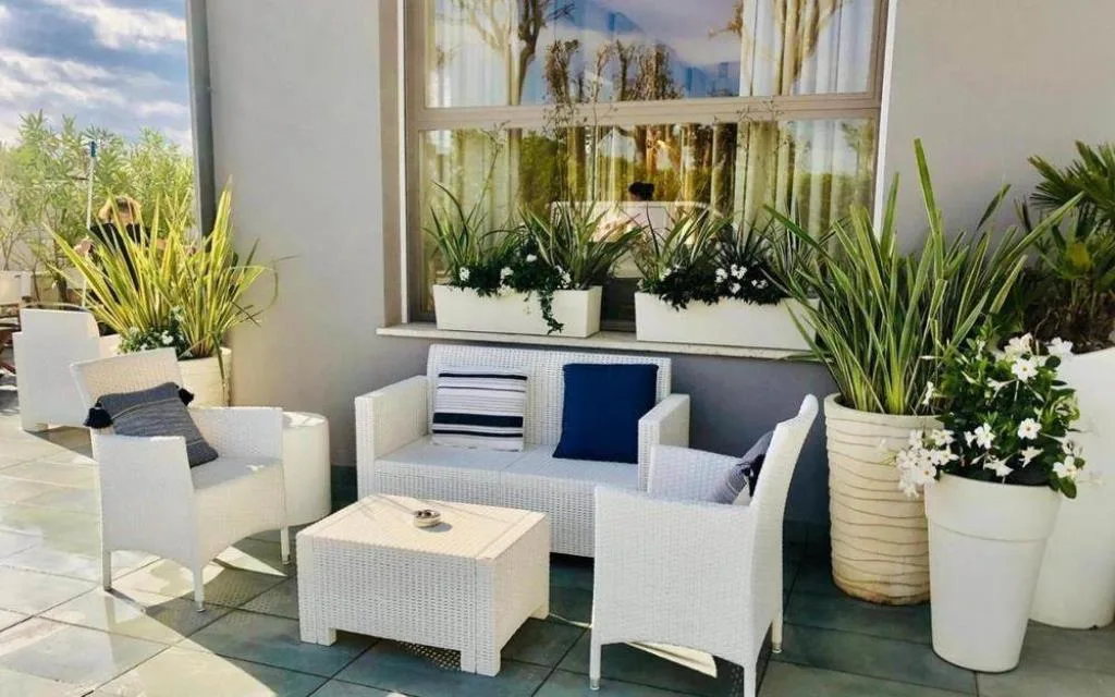 Salottino esterno con divani in rattan bianco e piante fiorite
