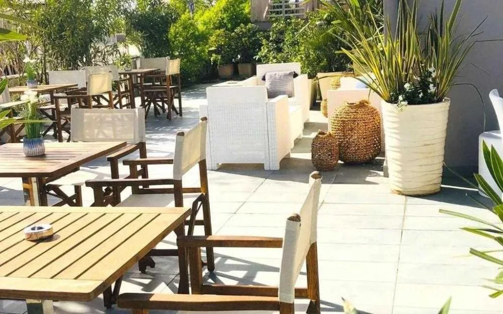 Terrazza soleggiata con tavoli in legno, sedie e piante ornamentali