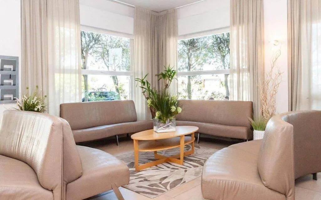 Salotto interno con poltrone beige, tavolino e grandi finestre luminose