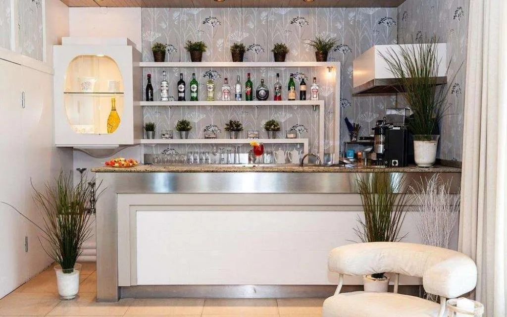 Bar dell'hotel con banco in acciaio, bottiglie e sgabelli bianchi