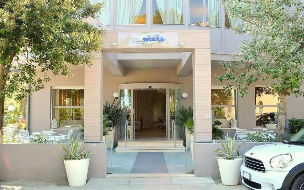 Ingresso dell'hotel Vì Mare con vetrata e alberi al sole
