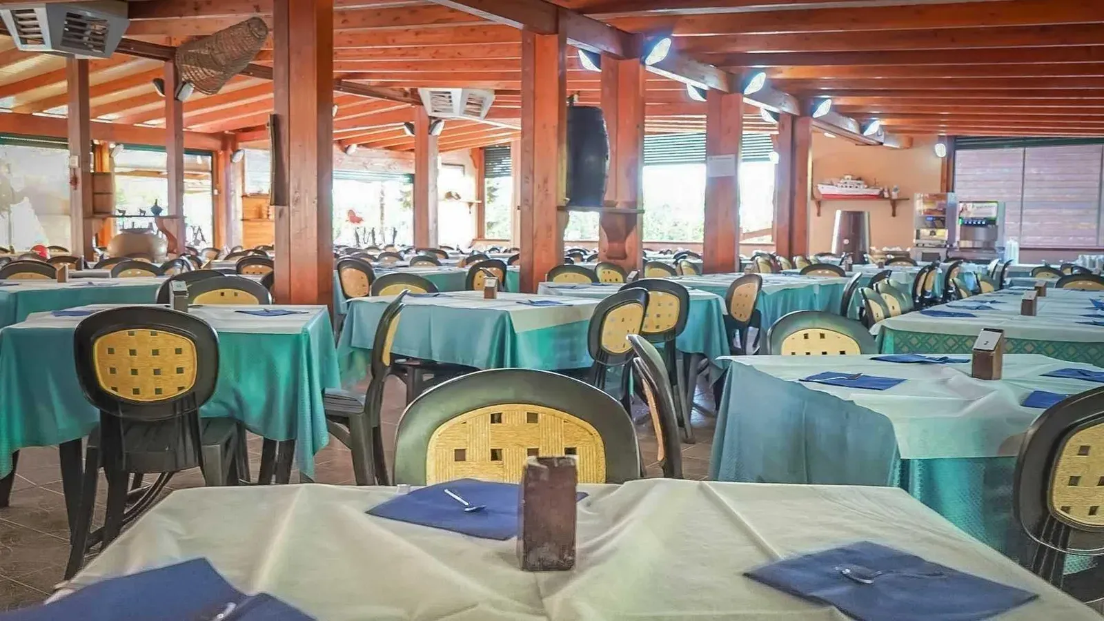 Ampia sala ristorante con travi in legno, tavoli apparecchiati e sedie