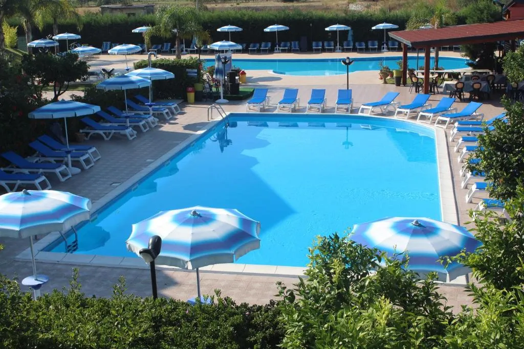 Piscina con ombrelloni a strisce, lettini blu e vegetazione attorno