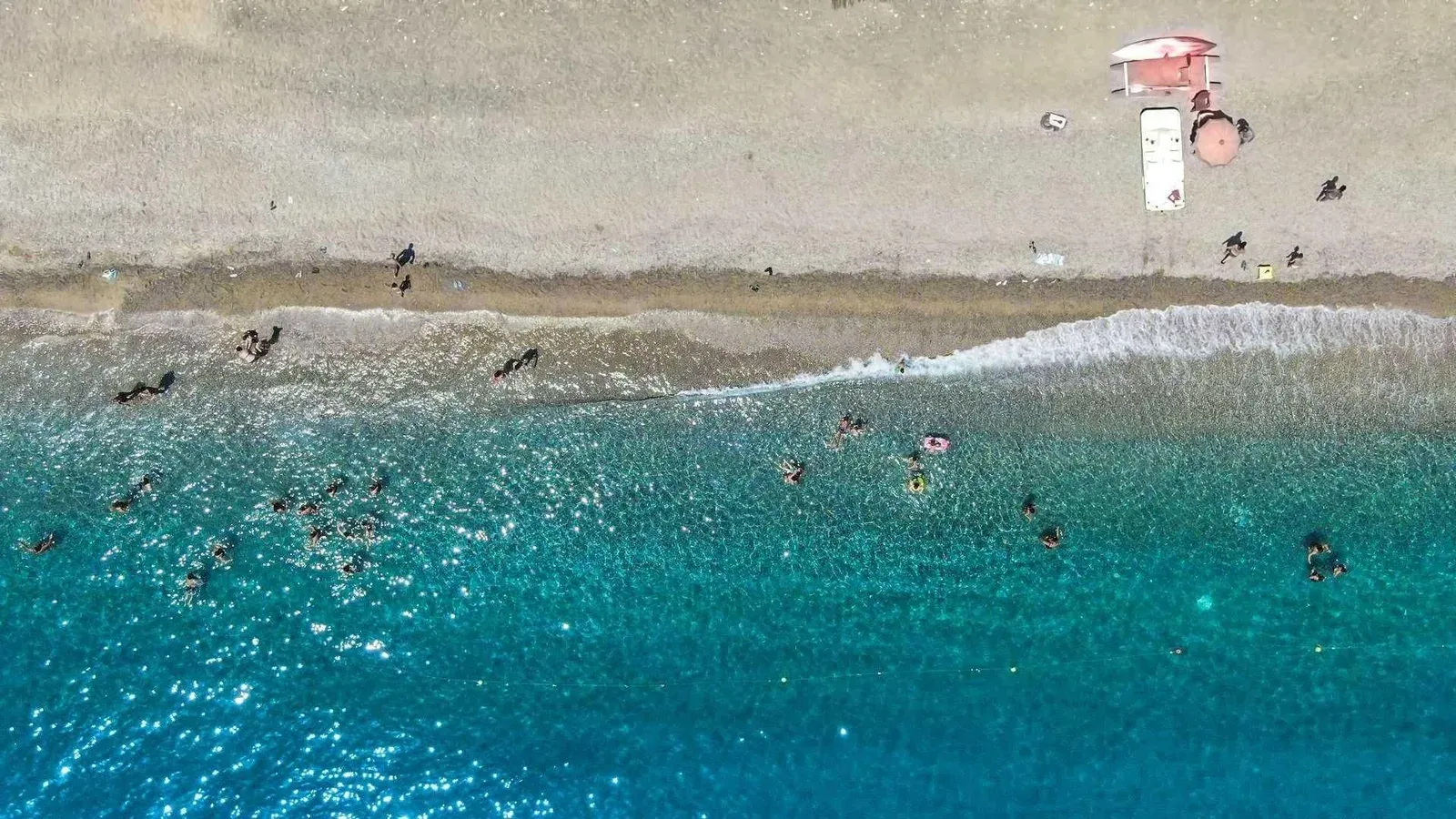 Vista aerea della battigia con bagnanti nel mare cristallino e ombrellone
